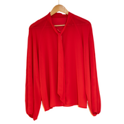 Coral chiffon shirtl loosely tied at the front pussy bow on a hanger.