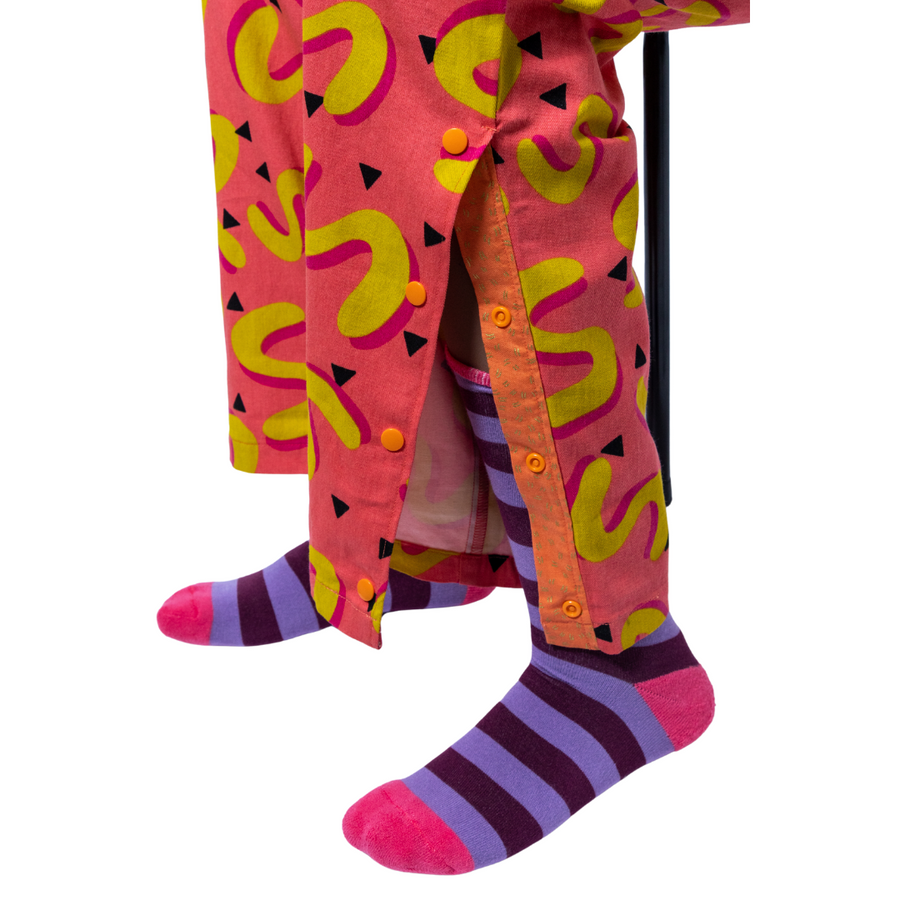 Close up of the 4 popper features on the bright pink, yellow and orange features. The model is sitting on a black stool and is also wearing purple and pink stripy socks